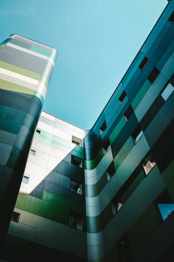 our-experience Low angle view of a modern building facade with green and blue panels under a clear sky.